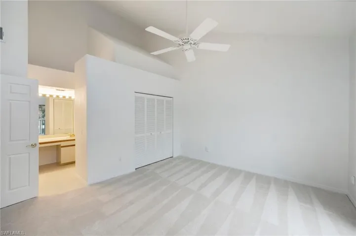 Unfurnished bedroom with light carpet, vaulted ceiling, a closet, ceiling fan, and ensuite bathroom