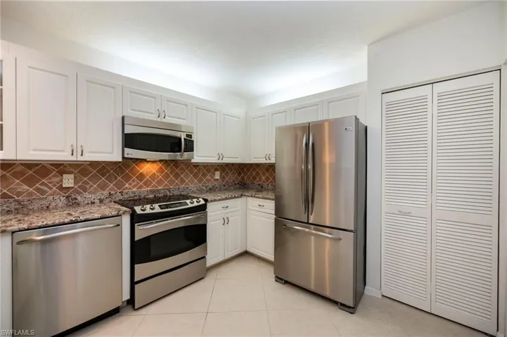 Kitchen with stainless steel appliances, dark stone counters, white cabinetry, light tile patterned floors, and decorative backsplash