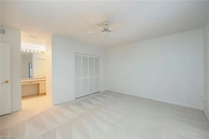 Unfurnished bedroom featuring a closet, ceiling fan, light colored carpet, and a desk
