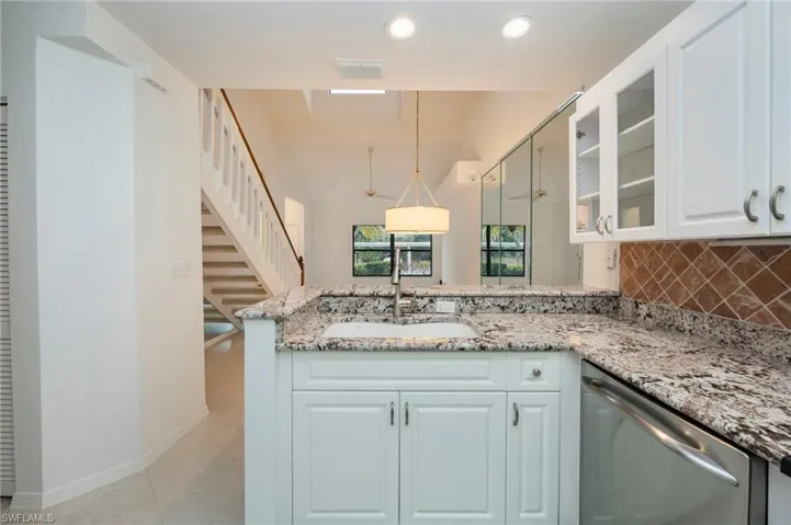 Kitchen with glass insert cabinets, a peninsula, light stone countertops, dishwasher, and white cabinetry
