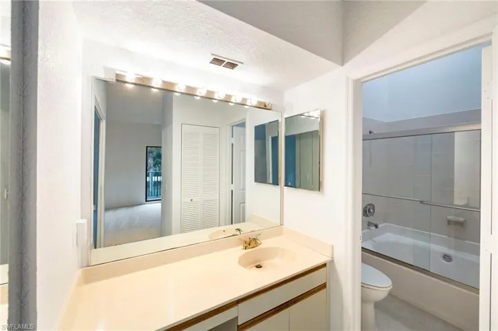 Bathroom with bath / shower combo with glass door, vanity, a textured ceiling, and a closet