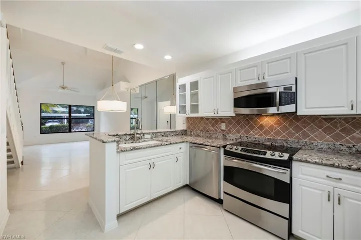 Kitchen featuring stainless steel appliances, pendant lighting, white cabinetry, light stone countertops, and vaulted ceiling