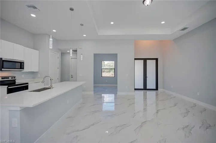 Kitchen featuring white cabinets, french doors, stainless steel appliances, an island with sink, and light stone counters
