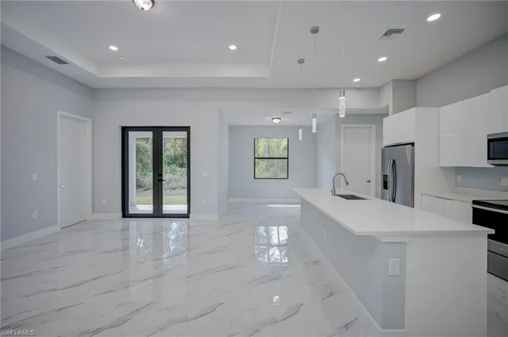 Kitchen with white cabinets, stainless steel appliances, open floor plan, french doors, and a kitchen island with sink
