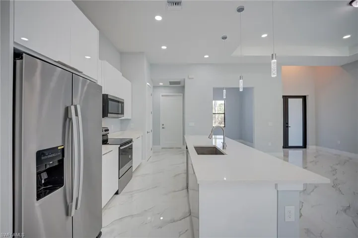 Kitchen featuring stainless steel appliances, an island with sink, white cabinets, decorative light fixtures, and light stone countertops