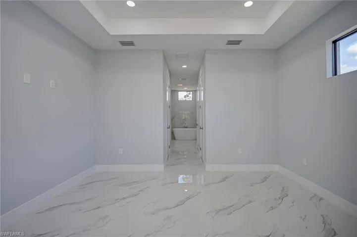 Unfurnished room featuring recessed lighting, light marble finish flooring, and a raised ceiling