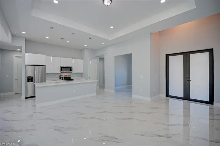 Kitchen with open floor plan, french doors, white cabinets, stainless steel appliances, and an island with sink