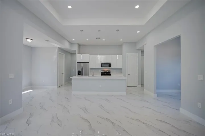 Kitchen with open floor plan, white cabinets, an island with sink, stainless steel appliances, and a raised ceiling