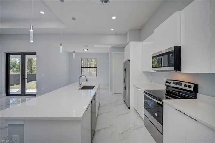 Kitchen with stainless steel appliances, a large island, light stone counters, white cabinetry, and hanging light fixtures
