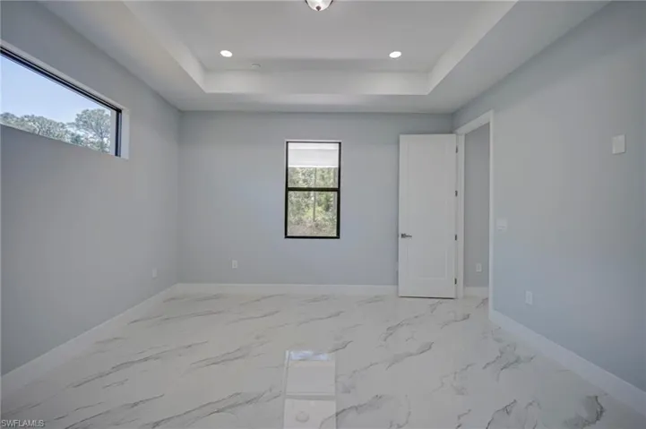 Spare room featuring light marble finish flooring, a raised ceiling, and recessed lighting