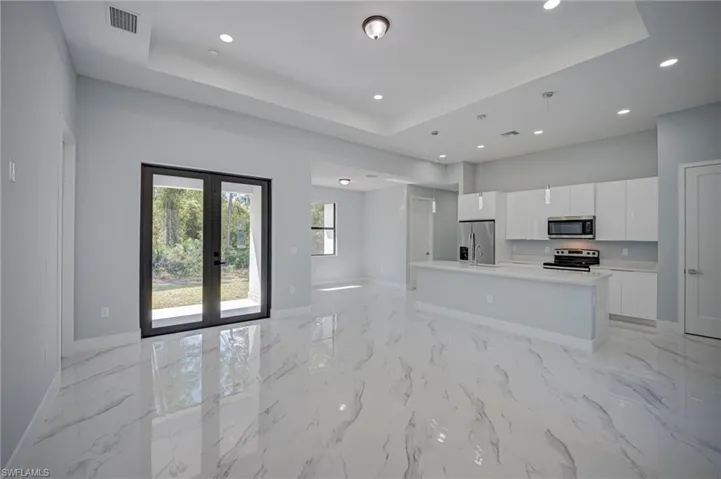 Kitchen featuring open floor plan, white cabinetry, an island with sink, french doors, and stainless steel appliances