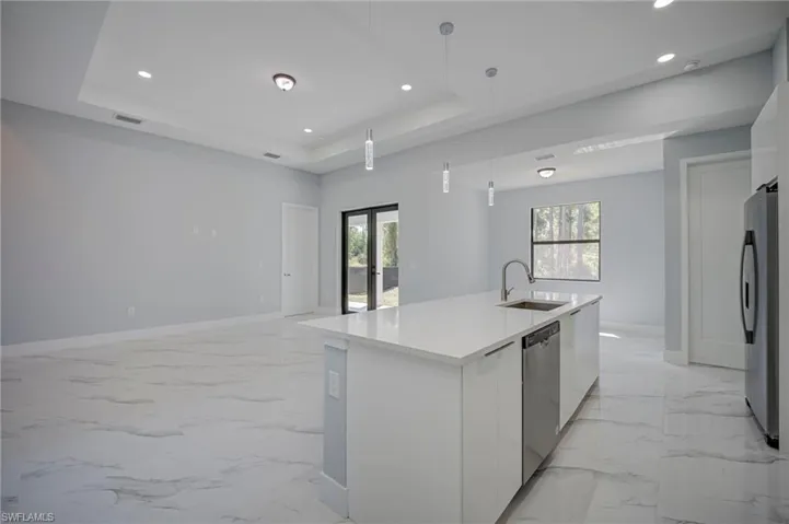 Kitchen featuring plenty of natural light, white cabinetry, a center island with sink, stainless steel appliances, and a tray ceiling