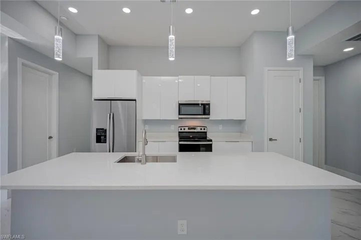 Kitchen featuring stainless steel appliances, pendant lighting, white cabinetry, and an island with sink