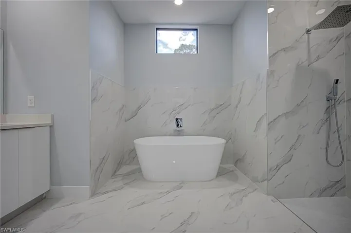 Bathroom with a marble finish shower, a freestanding tub, light marble finish floors, and vanity