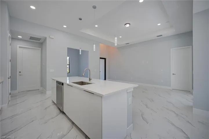 Kitchen with modern cabinets, white cabinets, light stone counters, hanging light fixtures, and a center island with sink