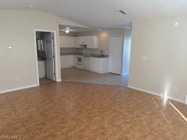 Kitchen featuring white cabinetry, open floor plan, white appliances, vaulted ceiling, and light tile patterned flooring