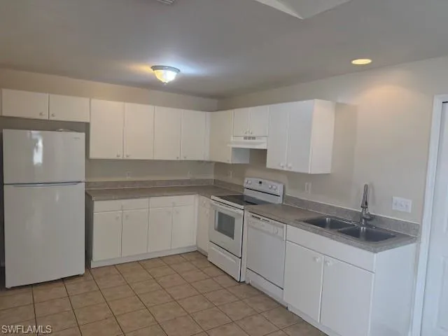 Kitchen featuring white appliances, white cabinets, under cabinet range hood, recessed lighting, and light tile patterned flooring