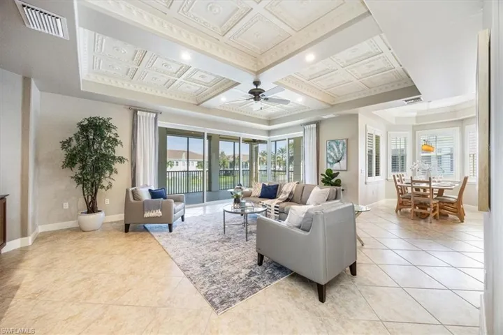 Tiled living room with crown molding, coffered ceiling, and ceiling fan