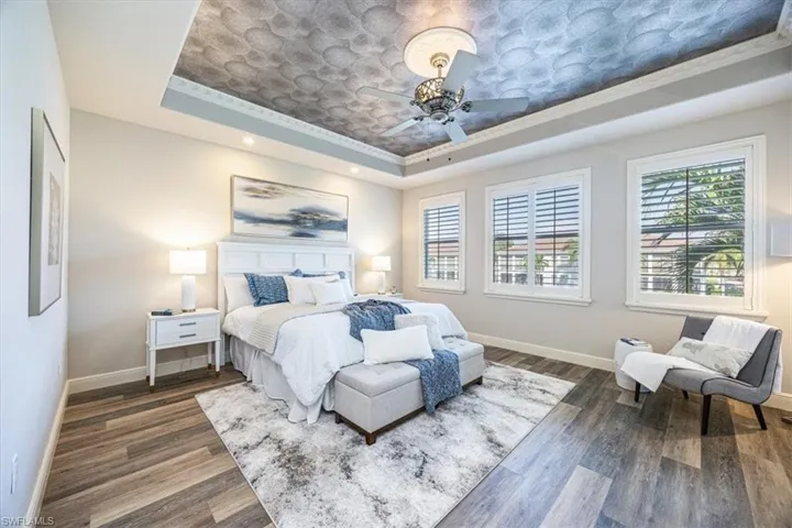 Bedroom featuring dark wood-type flooring, ceiling fan, a raised ceiling, and ornamental molding