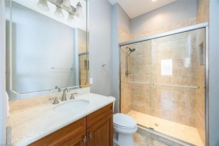 Bathroom with vanity, a shower with shower door, toilet, and tile patterned flooring