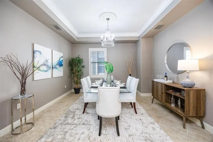 Tiled dining room featuring crown molding, a tray ceiling, and a chandelier
