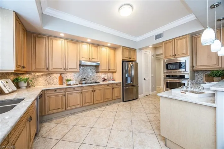 Kitchen with crown molding, pendant lighting, light tile patterned floors, appliances with stainless steel finishes, and tasteful backsplash