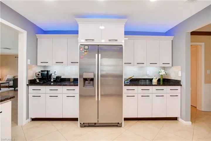 Kitchen featuring white cabinetry, stainless steel fridge with ice dispenser, tasteful backsplash, and dark stone counters