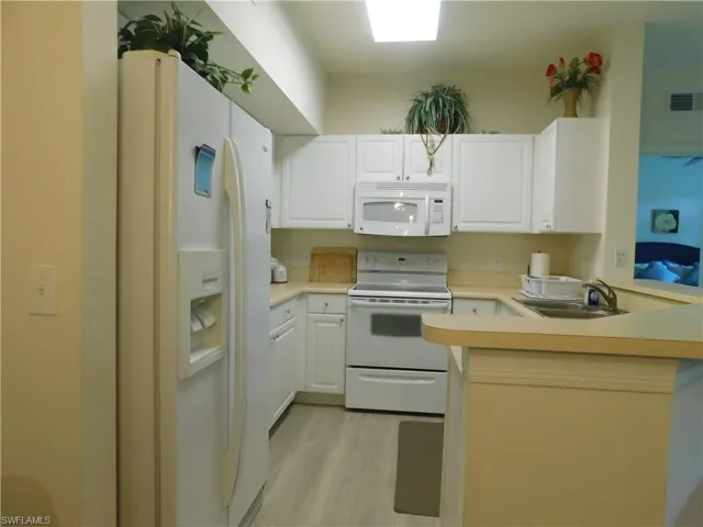 Kitchen featuring white cabinetry, white appliances, sink, light hardwood / wood-style floors, and kitchen peninsula
