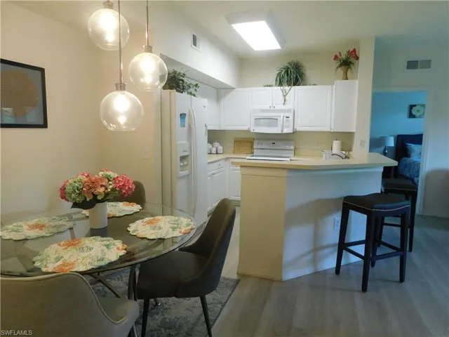 Kitchen featuring counter top bar, white cabinets, hardwood / wood-style flooring, decorative light fixtures