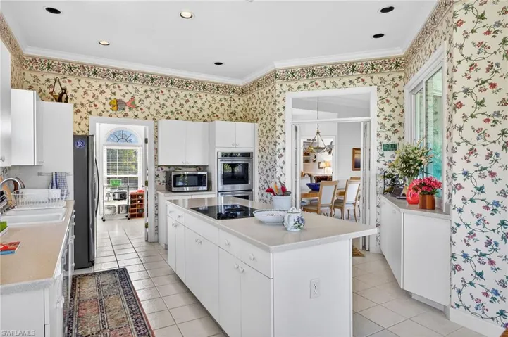 Kitchen featuring ornamental molding, white cabinetry, stainless steel appliances, a kitchen island, and light tile patterned flooring