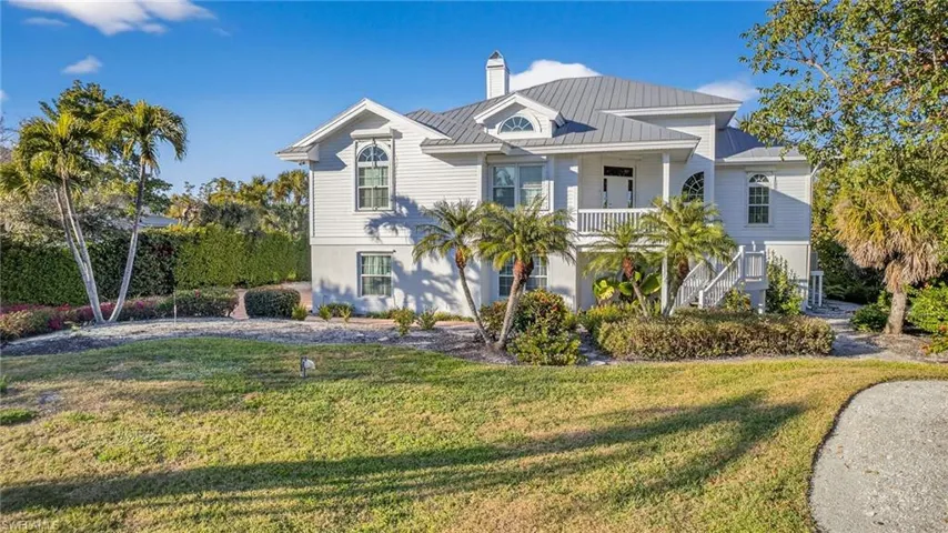 Coastal inspired home featuring a front lawn, a chimney, a metal roof, and covered porch