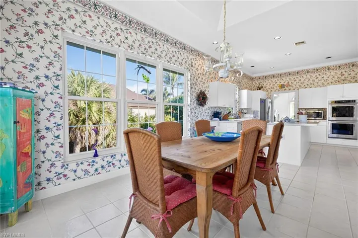 Dining area featuring wallpapered walls, healthy amount of natural light, ornamental molding, a chandelier, and light tile patterned floors