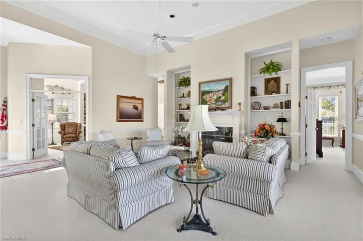 Living area featuring built in features, carpet flooring, crown molding, ceiling fan, and a glass covered fireplace