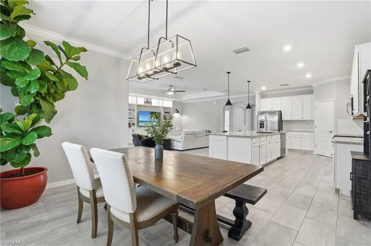Open-concept living space featuring a dining area with a rectangular wood-finish table, a kitchen island with pendant lighting, and white cabinetry