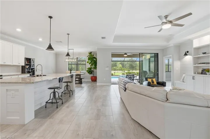 Open-concept living space featuring wood-finish flooring, a kitchen island with pendant lighting, white cabinetry, built-in shelving, and sliding glass doors opening to an outdoor area with a pool
