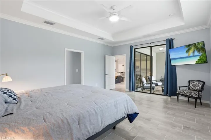 Spacious room featuring tray ceilings, crown molding, a ceiling fan with light fixture, and wood-look tile flooring