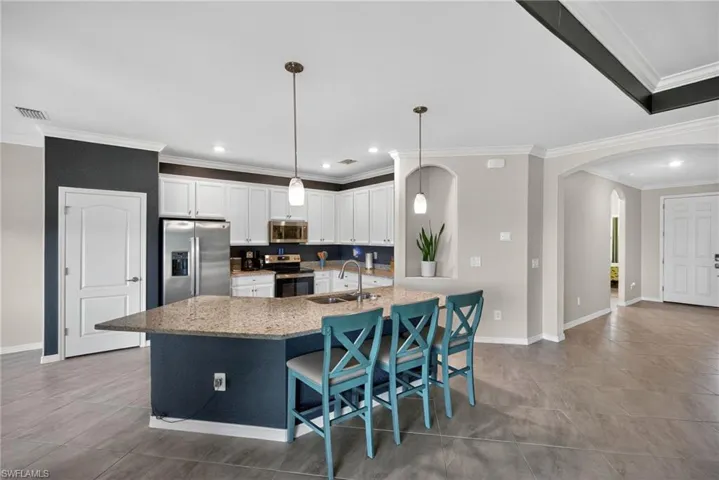 Kitchen featuring crown molding, stainless steel appliances, white cabinets, light stone countertops, and a kitchen breakfast bar