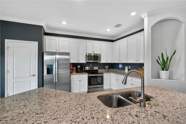 Kitchen featuring appliances with stainless steel finishes, white cabinets, light stone counters, crown molding, and recessed lighting
