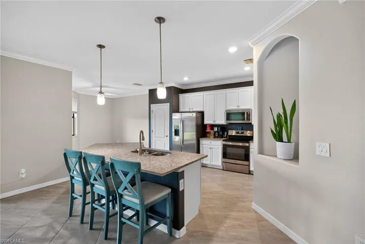 Kitchen with ornamental molding, stainless steel appliances, a kitchen breakfast bar, recessed lighting, and white cabinetry