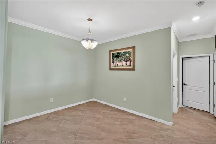 Empty room with ornamental molding, a chandelier, and light tile patterned floors