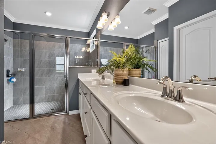 Full bath with double vanity, light tile patterned floors, a stall shower, and ornamental molding