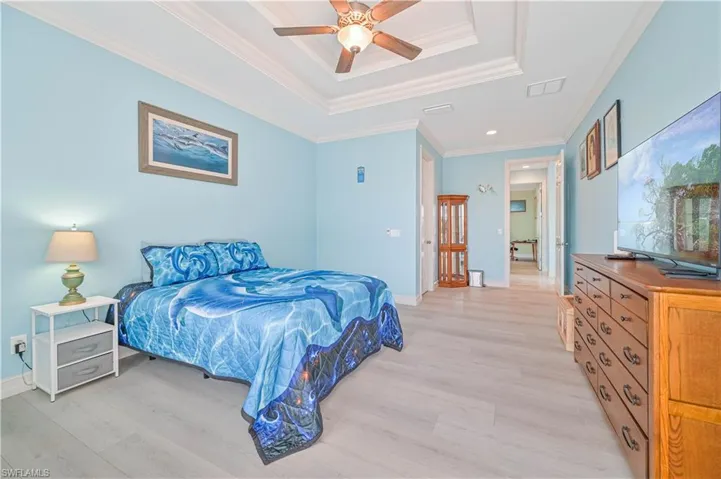 Bedroom featuring a tray ceiling, crown molding, light hardwood / wood-style flooring, and ceiling fan