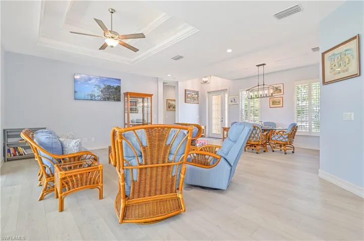 Living room with ceiling fan with notable chandelier, light hardwood / wood-style floors, and a raised ceiling