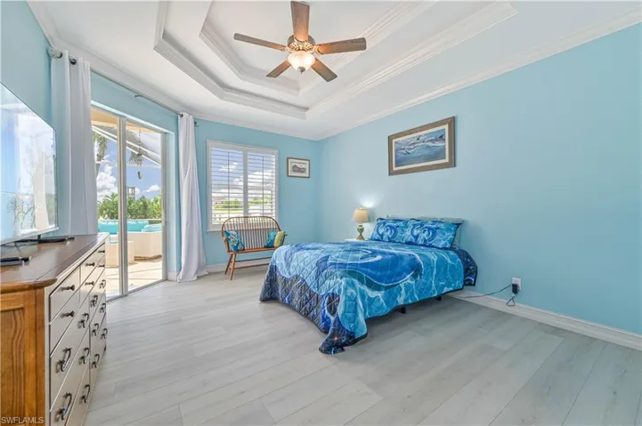 Bedroom featuring light hardwood / wood-style flooring, access to exterior, ceiling fan, a tray ceiling, and ornamental molding
