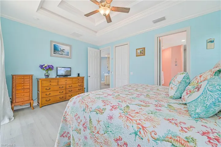 Bedroom featuring crown molding, ceiling fan, a tray ceiling, light hardwood / wood-style floors, and ensuite bath