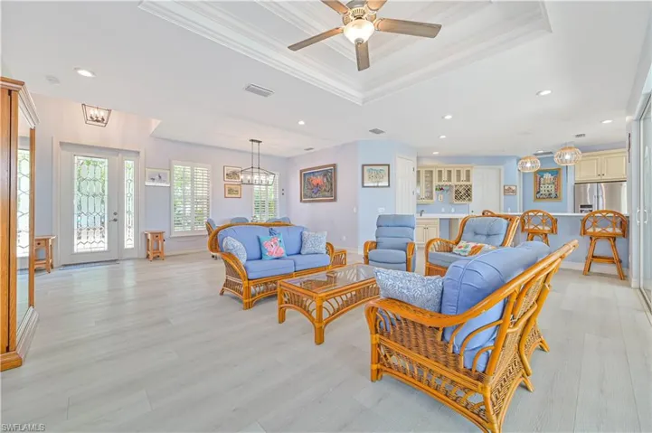 Living room with crown molding, ceiling fan with notable chandelier, a raised ceiling, and light hardwood / wood-style flooring