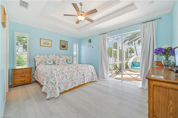 Bedroom featuring light hardwood / wood-style flooring, access to outside, a raised ceiling, and ceiling fan