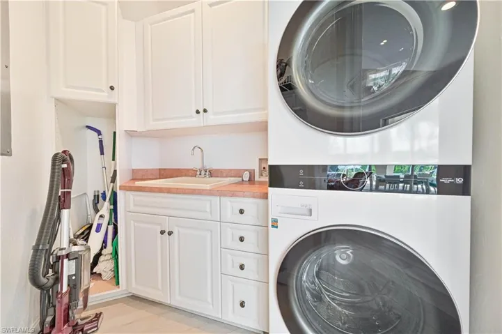 Laundry room featuring cabinets, stacked washer / dryer, light hardwood / wood-style flooring, and sink