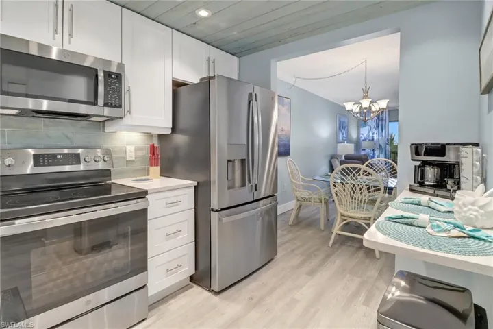 Kitchen with white cabinetry, a chandelier, stainless steel appliances, decorative backsplash, and light hardwood / wood-style floors