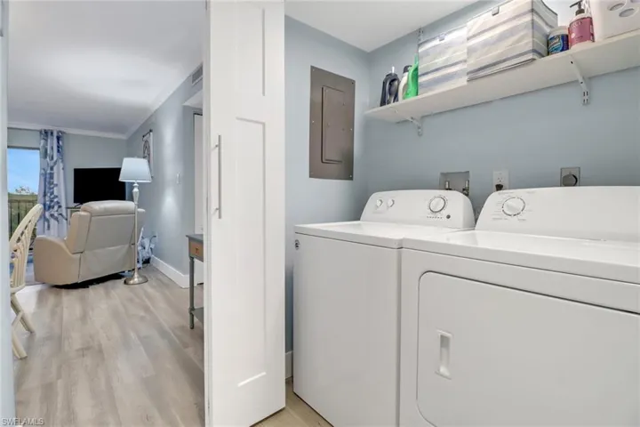 Laundry room featuring washing machine and clothes dryer, electric panel, light hardwood / wood-style flooring, and ornamental molding